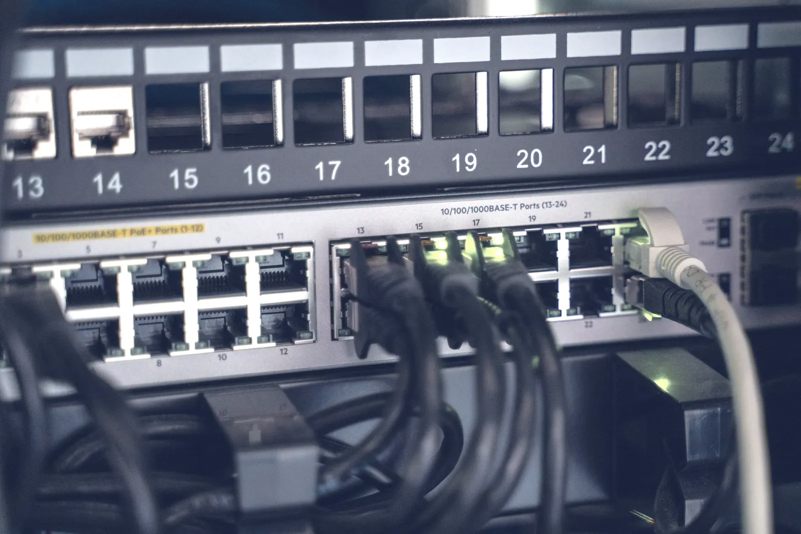 Patch panel numerado com cabos de rede ligados a um switch, em armário de rede
